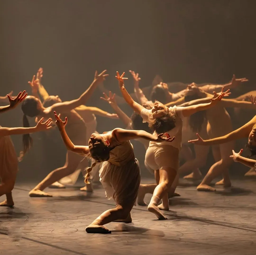 Large ensemble of dancers reaching upward in warm light