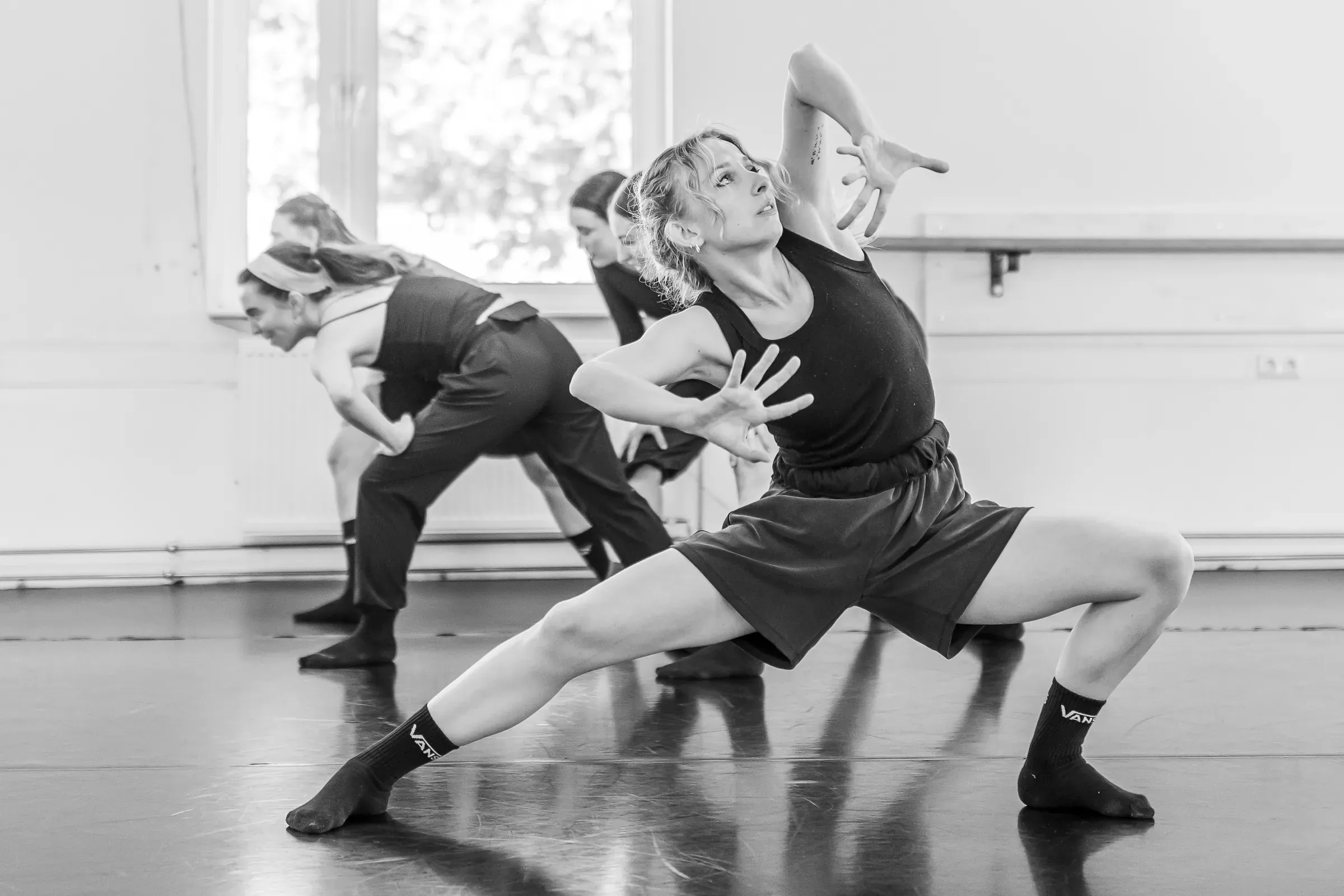 Lucie Marcellin in a lunge, arms raised, during a company rehearsal (black and white)