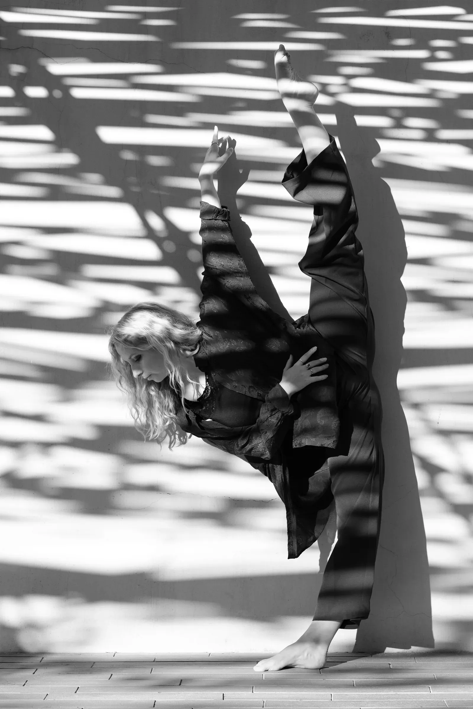 Lucie Marcellin with her leg raised vertically amid leaf shadows (black and white)