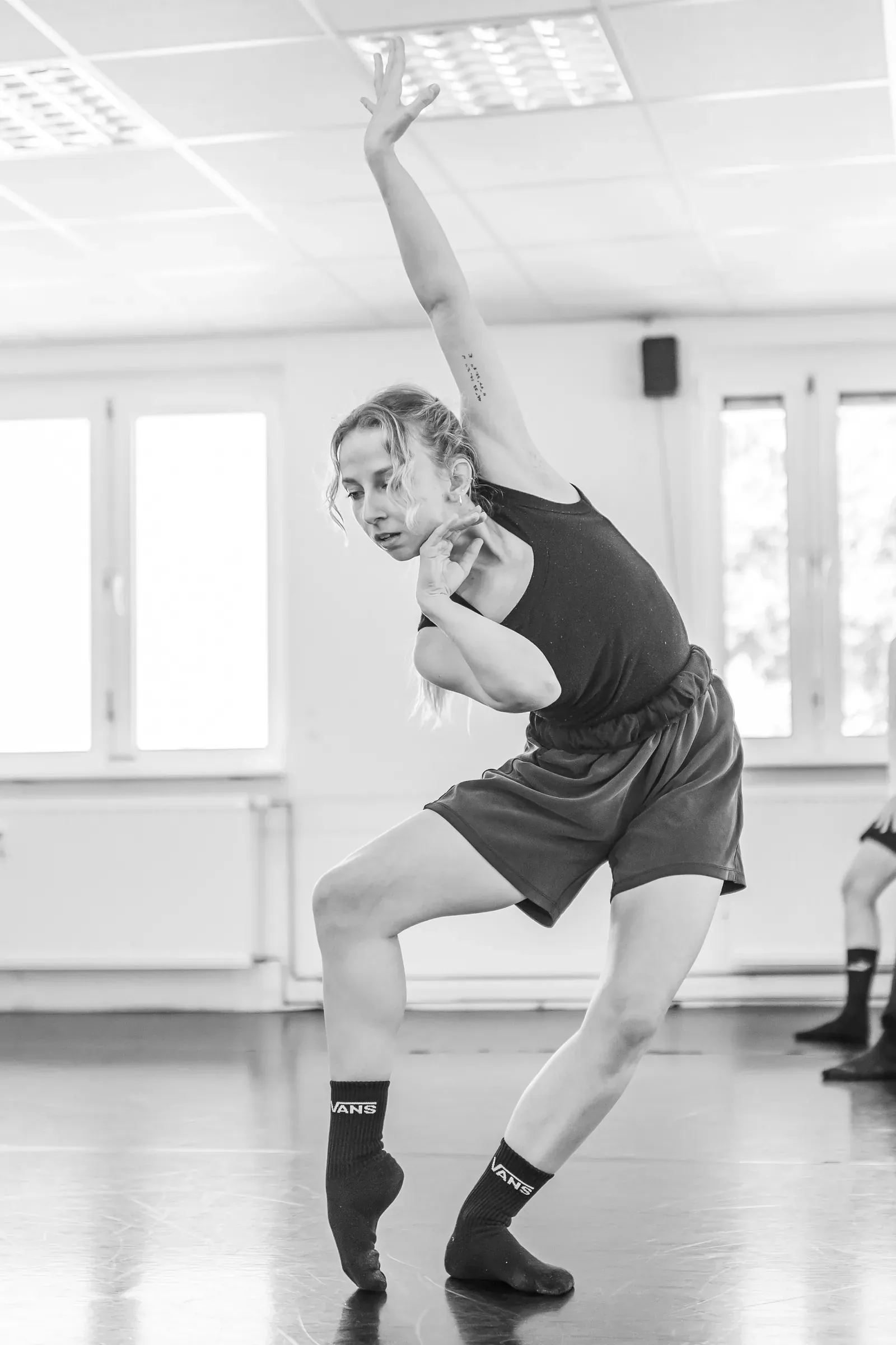 Lucie Marcellin twisting with one arm raised during rehearsal (black and white)