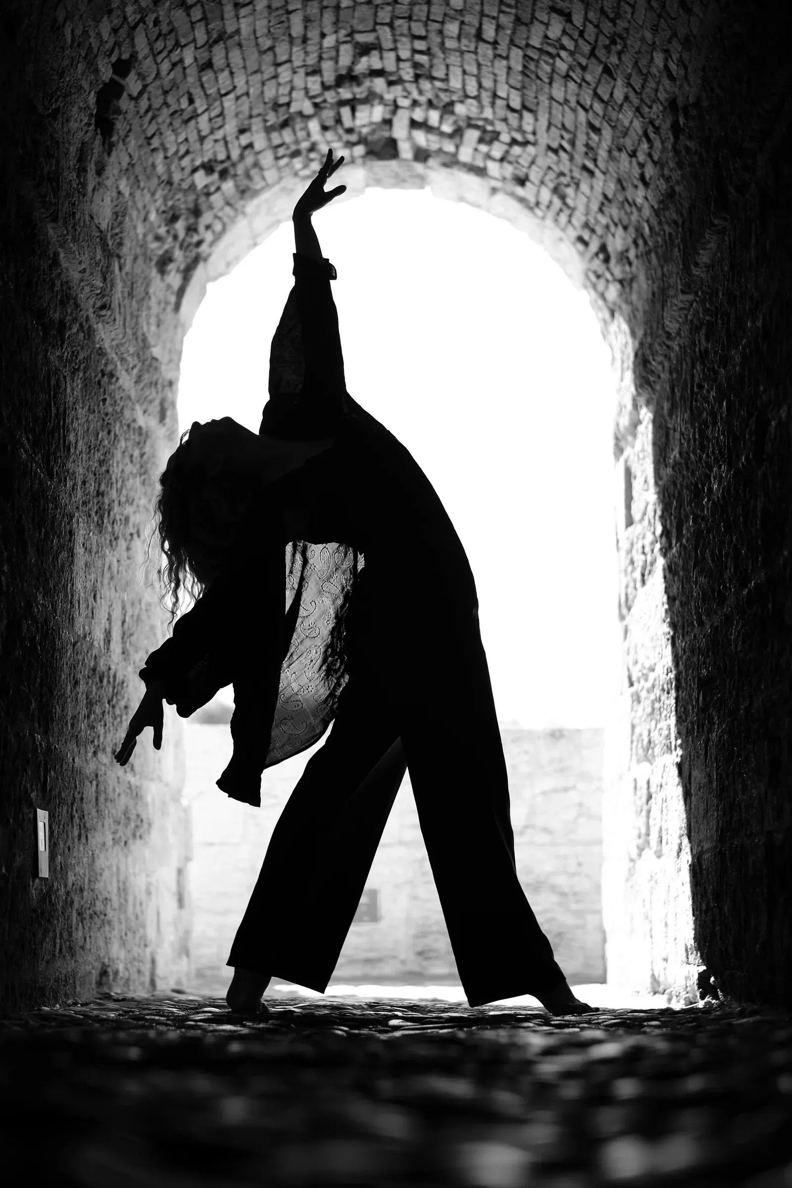 Silhouette of a dancer in a backlit stone tunnel (black and white)